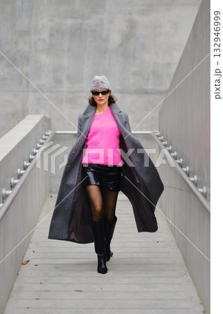 Model walks confidently in urban fashion featuring bright pink sweater and stylish coat 132946999