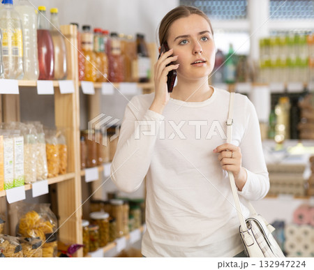 Girl shopping in grocery supermarket and talking on mobile phone Girl shopping in grocery supermarket and talking on mobile phone 132947224
