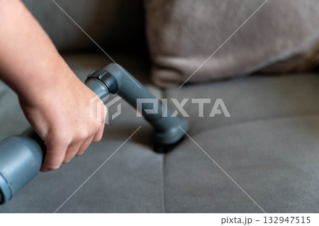 Hand holding vacuum cleaner attachment, cleaning gray fabric sofa, showcasing home maintenance and cleanliness, with focus on upholstery care and dust removal process Hand holding vacuum cleaner attachment, cleaning gray fabric sofa, showcasing home maintenance and cleanliness, with focus on upholstery care and dust removal process 132947515