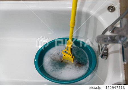 Cleaning tool submerged in a turquoise basin filled with soapy water, showcasing the process of maintaining hygiene in a bathroom environment with copy space Cleaning tool submerged in a turquoise basin filled with soapy water, showcasing the process of maintaining hygiene in a bathroom environment with copy space 132947518