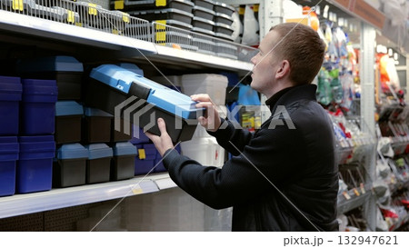 Man carefully choosing toolbox at hardware store, focusing on diy project. Shows handyman spirit in action. A man in a hardware store choosing a toolbox. Man carefully choosing toolbox at hardware store, focusing on diy project. Shows handyman spirit in action. A man in a hardware store choosing a toolbox. 132947621