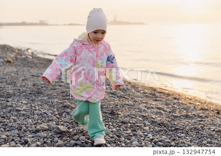 Child in warm clothes playing on a rocky beach at sunset Child in warm clothes playing on a rocky beach at sunset 132947754