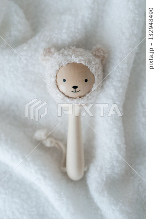 Minimal studio image of a wooden baby rattle on a white textured blanket, clean, soft aesthetic for newborn product listings and gentle lifestyle visuals 132948490