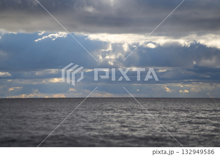 Overcast sky above calm sea horizon with sunlight filtering through clouds. Overcast sky above calm sea horizon with sunlight filtering through clouds. 132949586
