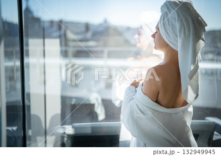 Back view of young woman with towel on her head looking out the window 132949945