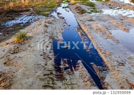 Water collects in muddy ruts, reflecting the damage caused by pollution and waste disposal in an ecological setting during daylight Water collects in muddy ruts, reflecting the damage caused by pollution and waste disposal in an ecological setting during daylight 132950099