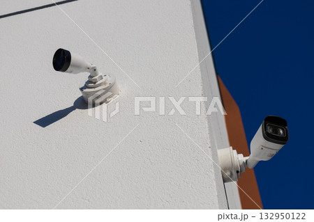 Two security cameras positioned on the side of a building monitor the surrounding area for safety and protection during daytime 132950122