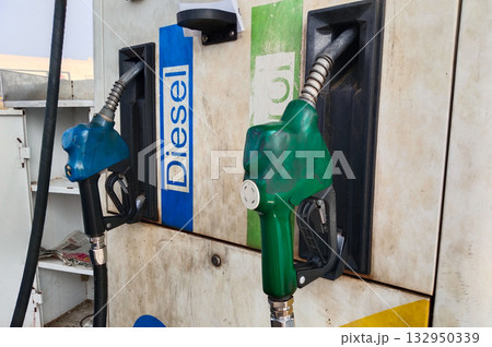 Close-up of diesel and petrol fuel pump nozzles at an Indian gas station, showing blue and green color-coded handles attached to dispenser machine with old paint and visible fuel pipes 132950339