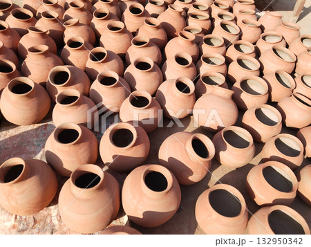 Freshly fired clay pots hand-painted with saffron color and sun-dried in open space for final setting, traditional Indian earthenware pottery placed for curing and long-term storage in sunlight. 132950342
