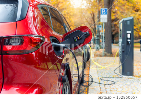 Close-up modern electric plug-in hybrid car SUV van parked fast charger charging station point center street old European city. Eco friendly green energy vehicle. Zero emission transport technology Close-up modern electric plug-in hybrid car SUV van parked fast charger charging station point center street old European city. Eco friendly green energy vehicle. Zero emission transport technology 132950657