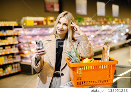 Customer using smartphone and shopping basket in supermarket Customer using smartphone and shopping basket in supermarket 132951288