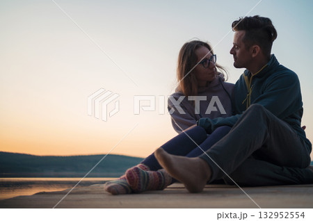 Couple Sitting by Lake at Sunset Embracing 132952554