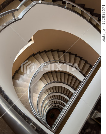 Spiral staircase viewed from above with curved metal railings and stone steps creating dramatic architectural symmetry 132952571