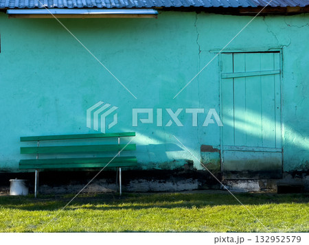 Bright turquoise wall with green bench and weathered door bathed in sunlight in a quiet yard 132952579