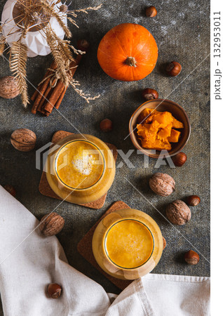 Autumn latte with pumpkin puree, nuts and cinnamon in glasses on the table top and vertical view 132953011