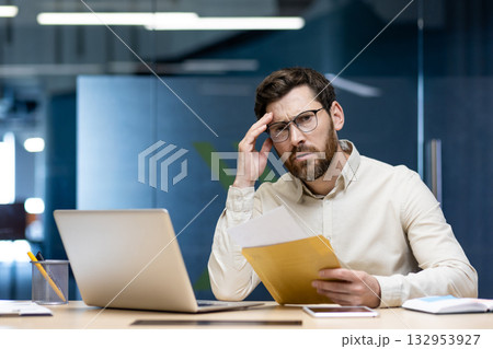 Portrait of upset and worried young businessman who received bad news and message by letter, holding envelope and looking at camera. Portrait of upset and worried young businessman who received bad news and message by letter, holding envelope and looking at camera. 132953927