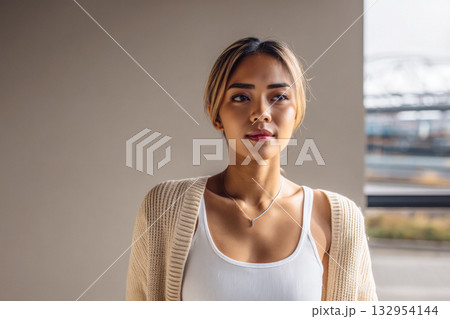 Young woman in cozy sweater looking thoughtfully out a window at a modern urban setting Young woman in cozy sweater looking thoughtfully out a window at a modern urban setting 132954144