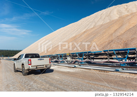 Bright sunlight illuminates open industrial potassium mining site blue conveyor structures silver pickup truck car dusty ground. Steel constructions contrast with light rocks and clear blue sky Bright sunlight illuminates open industrial potassium mining site blue conveyor structures silver pickup truck car dusty ground. Steel constructions contrast with light rocks and clear blue sky 132954214