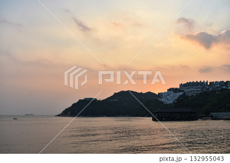 The seascape at sunset with ships and cityscape in the background. Sun-rays reflected on the calm sea. Sea background and cityscape. Nature concept. The seascape at sunset with ships and cityscape in the background. Sun-rays reflected on the calm sea. Sea background and cityscape. Nature concept. 132955043