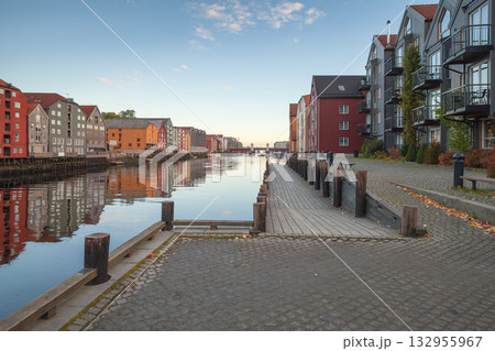 Vibrant rows of colorful houses line a tranquil canal, with a stone promenade 132955967