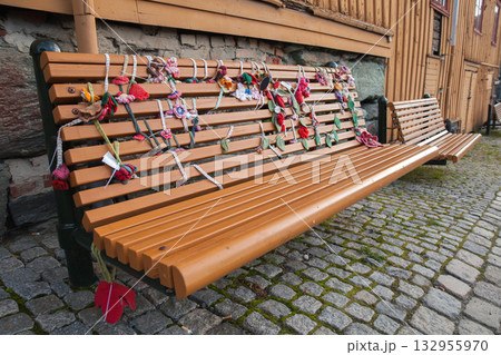 A long wooden bench sits on a cobblestone path beside a rustic building 132955970