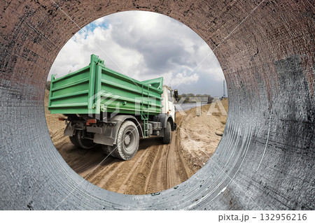 Heavy construction equipment is seen from a pipe, adding to the bustling activity on the site while clouds drift above in an open sky 132956216