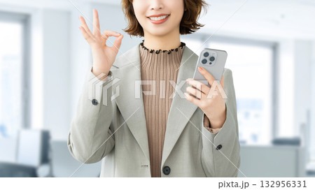 スマートフォンを持ってOKポーズをする笑顔の女性・ビジネスウーマン 132956331