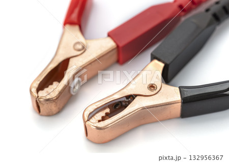 Close up of two alligator clips with red and black handles on white background, used for electrical connections. metal clamps are open, showing their teeth Close up of two alligator clips with red and black handles on white background, used for electrical connections. metal clamps are open, showing their teeth 132956367