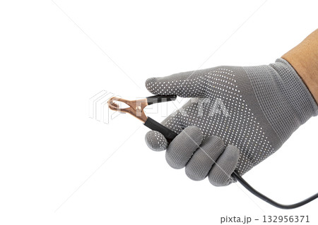 Hand in gray glove holds copper alligator clip with black cable on white background showing electrical safety and precision 132956371