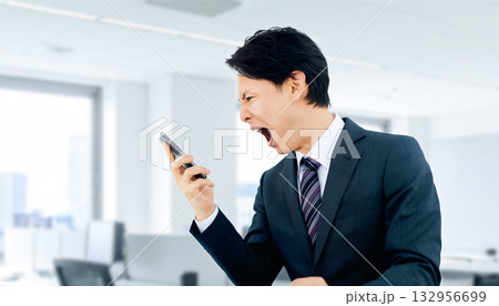 スマートフォンに向かって大声で怒る男性ビジネスマン スマートフォンに向かって大声で怒る男性ビジネスマン 132956699