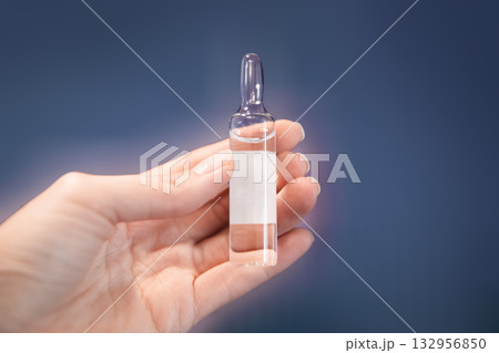 Woman's hand holds clear glass medicine ampoule 132956850