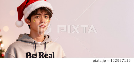 Young Asian man in a Santa hat with festive glitter makeup. Modern Christmas holiday portrait with copy space 132957113