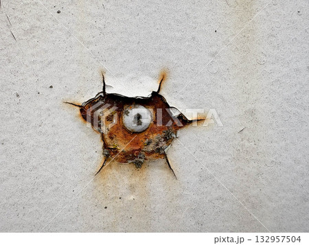 Aged metal texture. A rusty nail protrudes from beneath cracked white paint on a rusty metal surface. 132957504