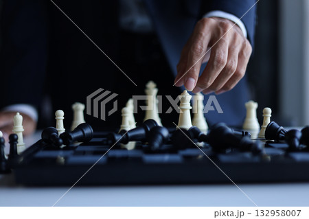 Businessman wearing suit, playing chess, game of strategy, leadership and management concept. 132958007