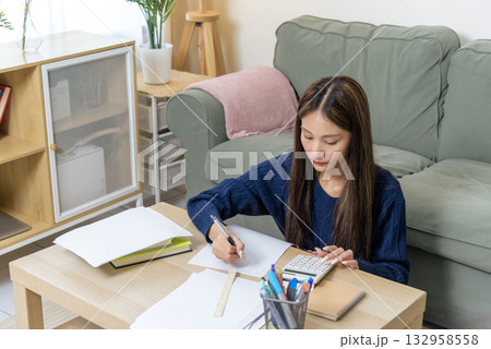 Teen girl doing homework, writing, studying for school, student focused on exam, show diligence, calculating numbers, preparing education assignment at home, demonstrating strong learning capability. Teen girl doing homework, writing, studying for school, student focused on exam, show diligence, calculating numbers, preparing education assignment at home, demonstrating strong learning capability. 132958558