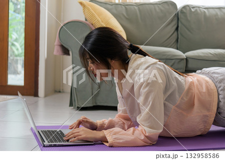 Healthy lifestyle woman teen maintaining health, exercising physical yoga home sport workout focused on laptop in bright comfortable living room. Healthy lifestyle woman teen maintaining health, exercising physical yoga home sport workout focused on laptop in bright comfortable living room. 132958586