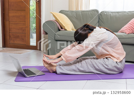 Healthy lifestyle, young woman teen doing physical yoga exercise workout at home, stretching body on purple exercise yoga mat, watching laptop for flexible fitness routine. Healthy lifestyle, young woman teen doing physical yoga exercise workout at home, stretching body on purple exercise yoga mat, watching laptop for flexible fitness routine. 132958600