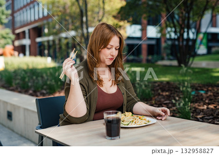 Plus size woman having lunch outdoors, eating noodles. 132958827