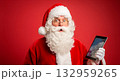 Santa Claus looking surprised while holding a tablet on a red background 132959265