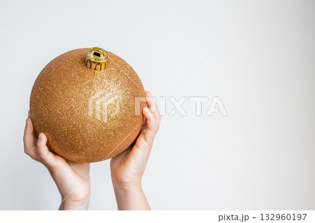 Child hands holding large golden Christmas ornament against white background 132960197