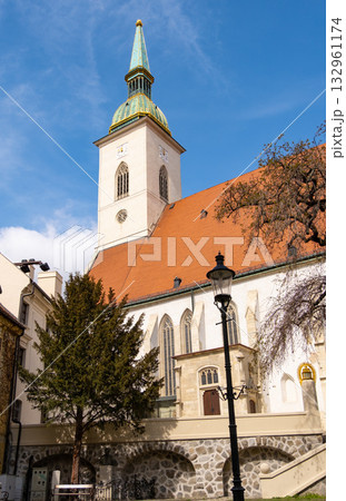 St. Martin's Cathedral stands prominently against the Bratislava skyline, showcasing its historical architecture. Nearby buildings and a clear sky add to the urban landscape's charm 132961174