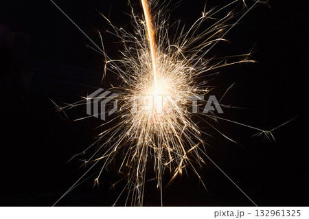 Sparkler Firework. Close-up of a bright sparkler emitting golden sparks against a dark background. 132961325
