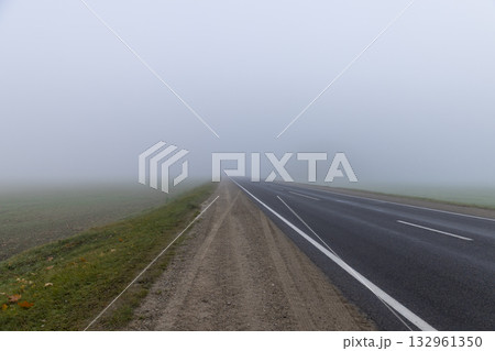 paved road in the autumn season in cloudy weather with thick fog, highway with poor visibility due to fog 132961350