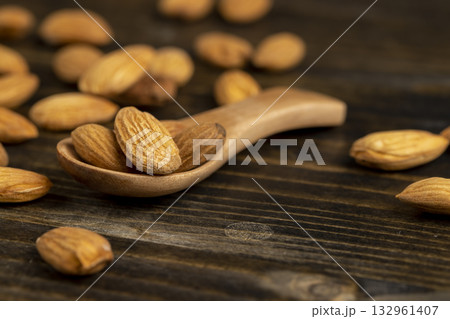 whole nuts of unroasted almonds with a wooden spoon on the table, a large number of hard raw almonds on the table during cooking 132961407