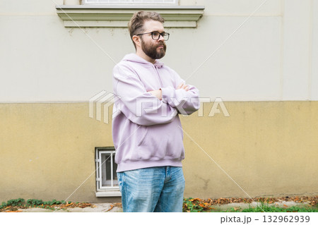 Sad man standing near building wall with folded arms. Copy space and empty place for advertising. Confidence, isolation, and personal reflection. Sad man standing near building wall with folded arms. Copy space and empty place for advertising. Confidence, isolation, and personal reflection. 132962939