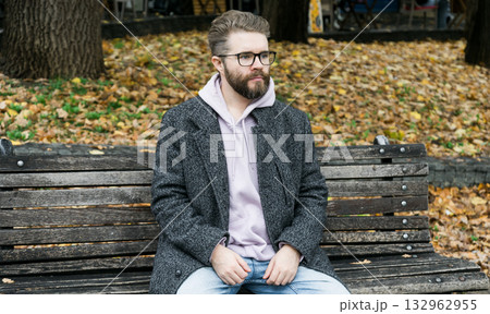 Man sitting on park bench in autumn leaves. Copy space and empty place for advertising. Calm atmosphere, reflection, and urban relaxation. Man sitting on park bench in autumn leaves. Copy space and empty place for advertising. Calm atmosphere, reflection, and urban relaxation. 132962955
