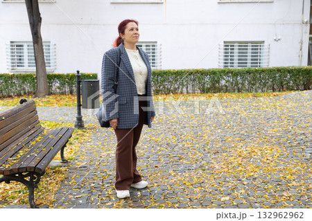 Woman standing on street covered with fallen leaves. Copy space and empty place for advertising. Autumn nostalgia, quiet reflection, and gentle solitude in city life. Woman standing on street covered with fallen leaves. Copy space and empty place for advertising. Autumn nostalgia, quiet reflection, and gentle solitude in city life. 132962962