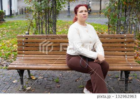 Woman sitting on wooden park bench in autumn park. Copy space and empty place for advertising. Reflection, calm presence, and emotional clarity in nature. Woman sitting on wooden park bench in autumn park. Copy space and empty place for advertising. Reflection, calm presence, and emotional clarity in nature. 132962963