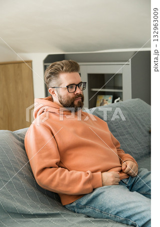 Man sitting on sofa and looking ahead. Moment of stillness symbolizing contemplation, patience, inner focus and everyday thinking at home interior. Man sitting on sofa and looking ahead. Moment of stillness symbolizing contemplation, patience, inner focus and everyday thinking at home interior. 132963009
