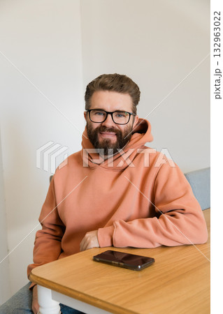 Man smiling at camera in casual hoodie. Representation of friendliness, trust, openness and approachable character during relaxed communication at home or workplace. Man smiling at camera in casual hoodie. Representation of friendliness, trust, openness and approachable character during relaxed communication at home or workplace. 132963022